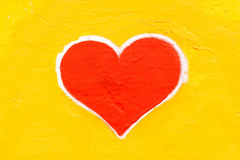 Red heart spray painted on a yellow wall.